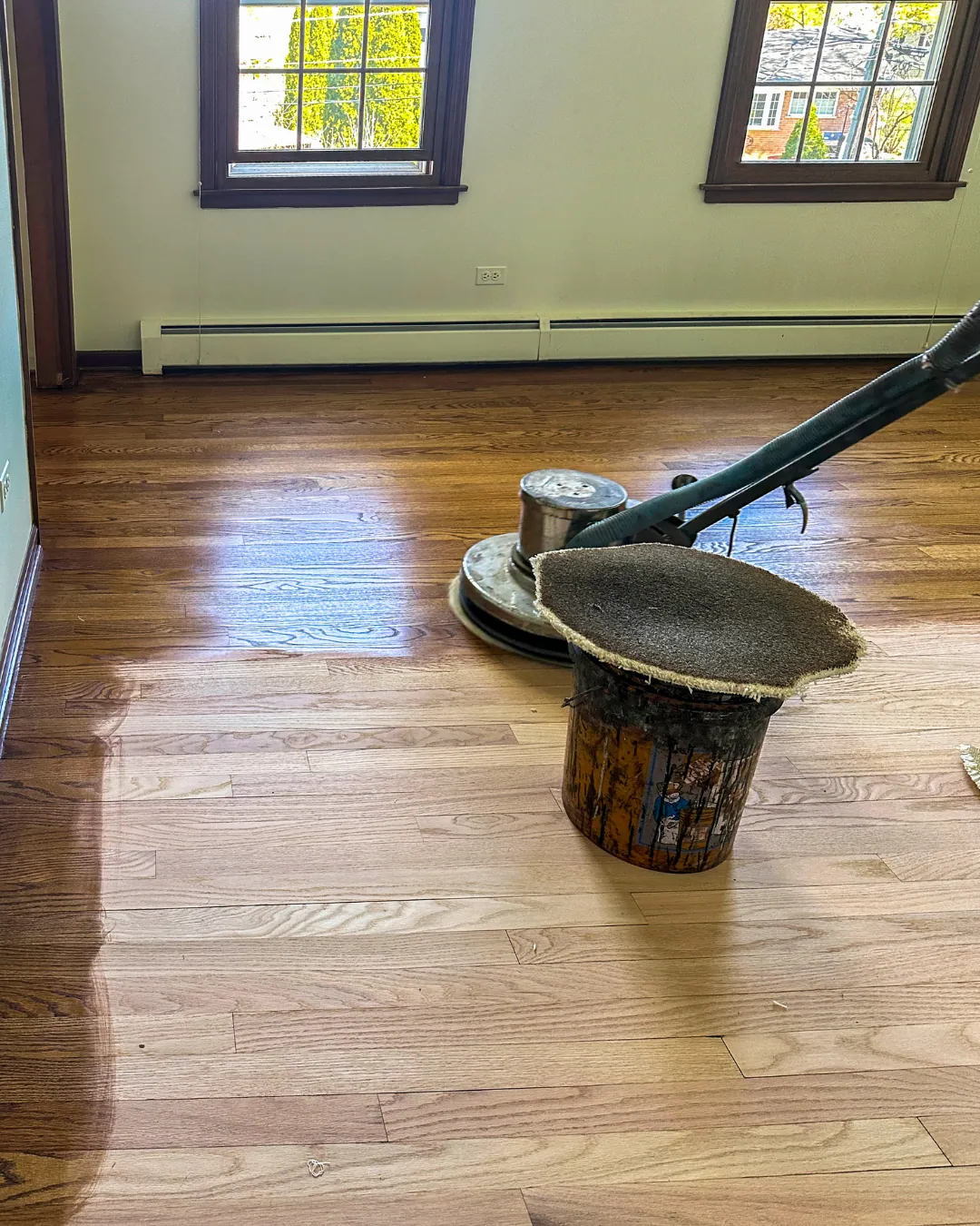 Oak strip hardwood floor partway through refinishing, with freshly sanded boards beside the old darker finish